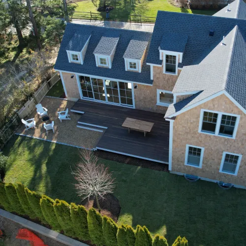 Aerial view of a shingled home with dormers and patio